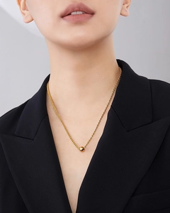 Close-up of a gold bead pendant on a titanium steel necklace worn on the collarbone