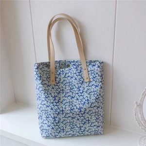 Detail of floral tote bag with blue patterns, leather handles and magnetic closure buckle