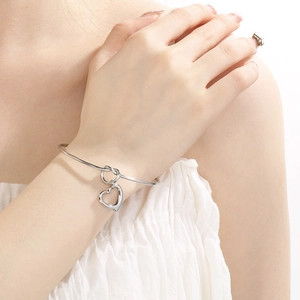 Close-up of a silver stainless steel open bangle featuring a heart charm on a wrist