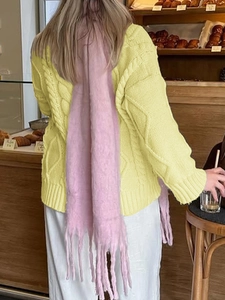 Women's yellow cable knit cardigan sweater paired with a long pink tassel scarf