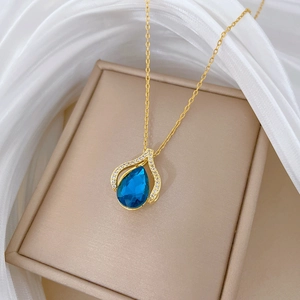 Detail of gold necklace with blue teardrop pendant and pavé crystals on silk background