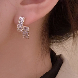 Detail view of long gold fringe earrings with rectangular zircon on model ear