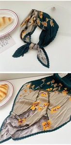 Detail of pleated dark green floral silk scarf with zigzag edges and elegant draping