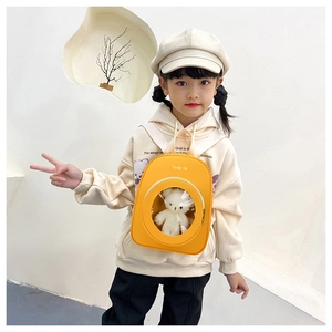 Detail of yellow kids backpack with clear window and plush bear inside, worn crossbody