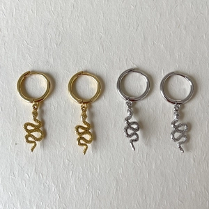 Detailed view of textured snake-shaped drop earrings in gold and silver finishes