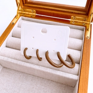 Detailed view of four brown C-shaped hoop earrings displayed inside a wooden jewelry box