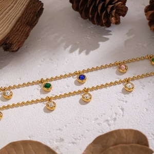 Close-up of golden beaded chain with colorful zircon pendants on white textured surface