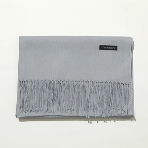 Detail shot of a light gray cashmere scarf with a premium tassel fringe and brand label