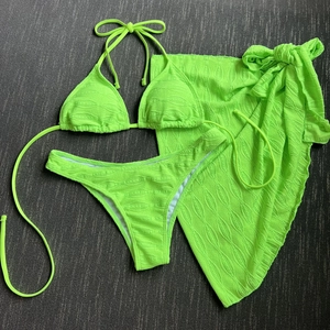 Flat lay of neon green three-piece bikini with textured fabric and matching sarong