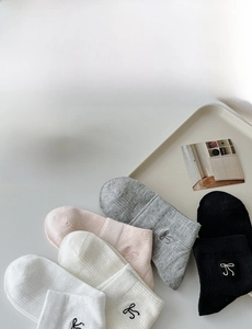 Detail of white cotton bow socks with vertical ribs shown in five soft colors on a tray