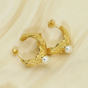 French style gold plated C-shaped earrings with white pearl detail on beige fabric