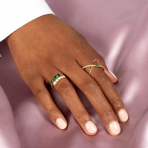 Close-up of stacked gold rings with emerald stones on a pink silk background