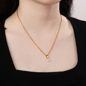 Close-up of a minimalist golden chain necklace with a small white pearl pendant on a model