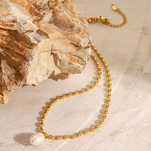 Détail d'un collier de perles dorées sur pierre beige avec chaîne perlée et fermoir