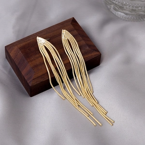 Close-up of golden tassel earrings with snake bone chains on a premium silk background