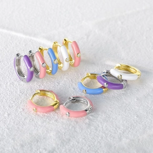 Detail of colorful enamel hoop earrings with inlaid diamonds on a white textured surface