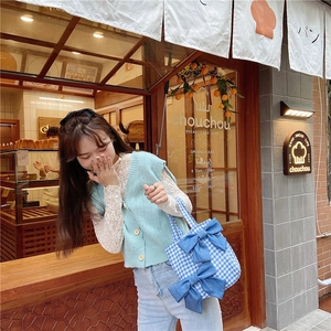 Detail of blue plaid canvas tote bag with large denim bows against a cafe background