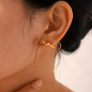 Detail of 18k gold plated bowknot stud earrings with tassels on a model's ear