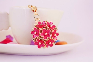 Detail of rose red enamel daisy keychain with gold metal plating on a white ceramic cup