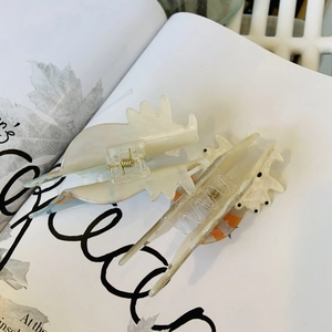 Detailed shot of cream acrylic hair claw clips with orange ink patterns on a book