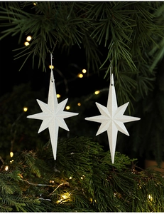 Detail of two white star Christmas tree ornaments with silver glitter on pine branches