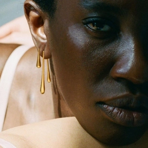 Close-up of golden teardrop tassel earrings worn by a model with artistic lighting