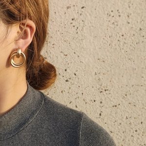 Macro detail of matte gold double-intertwined geometric earrings on model's ear