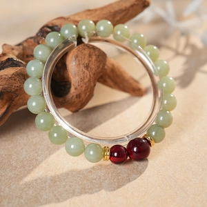 Detailed close-up of natural jade beads bracelet with red agate and gold accents on wood