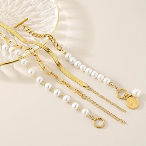 Detail of four-piece layered gold bracelets with pearls and coin pendant on glass