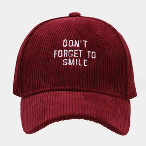 Macro shot of white Don't Forget To Smile embroidery on burgundy corduroy baseball cap