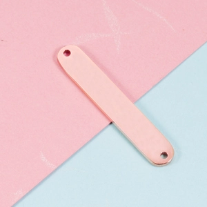 Detail van een roségouden rechthoekige metalen bedel met twee gaten voor DIY-sieraden