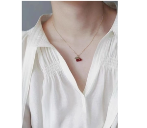 Detail of red cherry pendant necklace with green leaves on minimalist metal chain