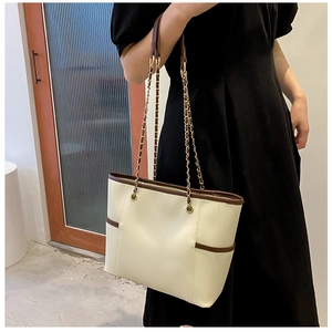 Detail of cream tote bag featuring brown edge trim and metal chain interwoven shoulder strap