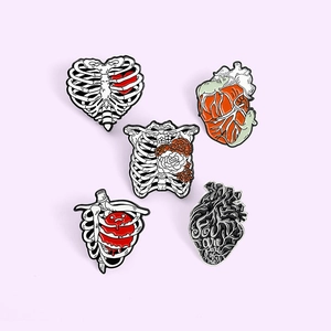 Detailed set of 5 anatomical heart and rib cage enamel pins on a soft pink background