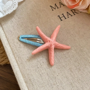Detail showing a pink starfish hair clip with blue woven fabric wrap on metal duckbill clip
