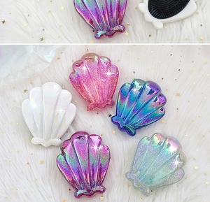 Detailed view of colorful shell-shaped glitter hairbrushes on white velvet fabric