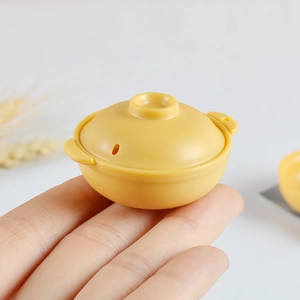 Miniature yellow dollhouse cooking pot toy shown in hand for scale comparison