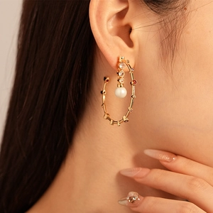 Close-up of golden bamboo circle earring with colorful stones and white pearl on model