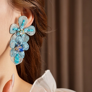 Detailed close-up of blue embroidered floral earrings with beads and sequins on a model