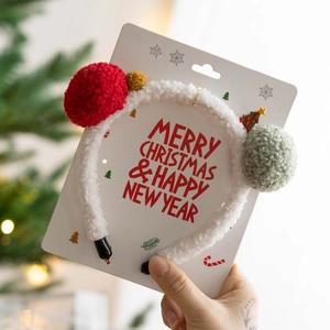 Close-up of a white plush Christmas headband with red pom-poms and small tree ornaments