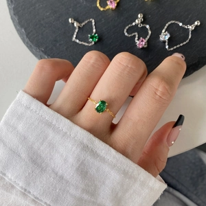 Close-up of gold chain ring featuring an oval green emerald in a four-prong setting