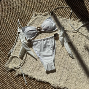 Detailed macro of white bikini featuring gold shell hardware on textured fabric
