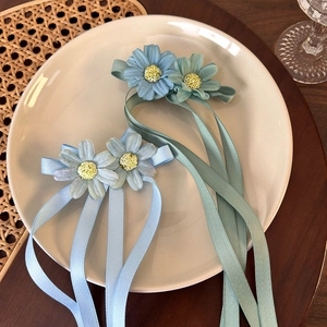 Detailed view of daisy flower hair clips with long sky blue and mint green ribbons