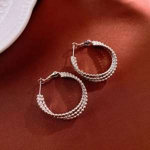 Detail view of silver multi-layer textured hoop earrings on a dark red satin background