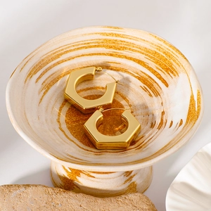 Minimalist hexagonal gold hoop earrings placed in an artistic ceramic dish setting