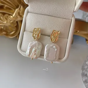 Detailed macro view of baroque rectangle pearl earrings with textured gold metal accents