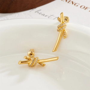 Elegant gold knot stud earrings featuring sparkling pavé zircon on a white ceramic stand
