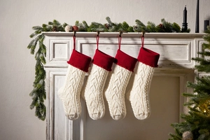 Detail of red and white chunky knit Christmas stockings hanging on a white fireplace mantle