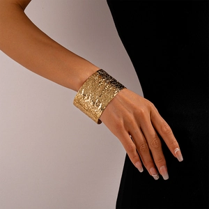 Detail of wide gold cuff bracelet featuring irregular hammered metal texture for women