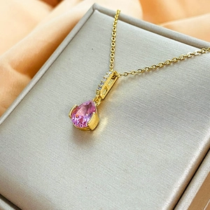 Dettaglio di un ciondolo in zircone rosa a goccia su una collana dorata in acciaio al titanio